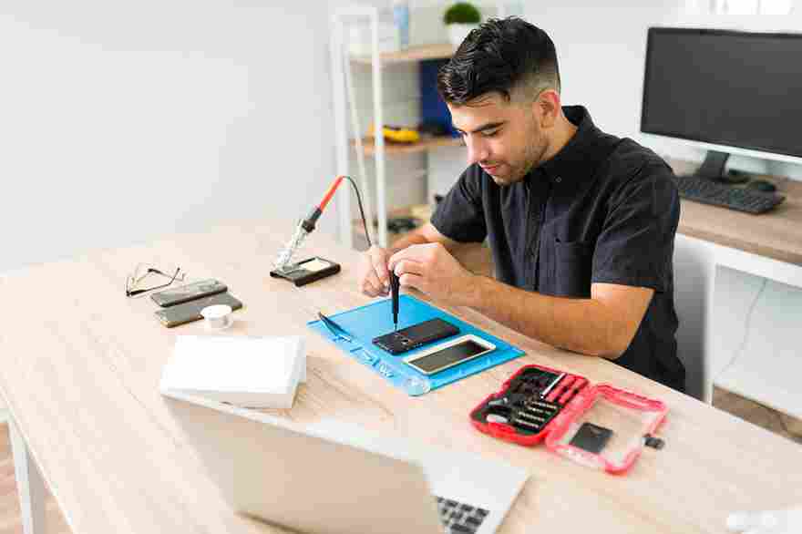 A smiling technician repairing a smartphone at a clean, organized workshop using a screwdriver and professional tools.