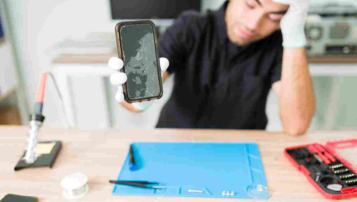 Upset male technician showing a cracked smartphone screen.